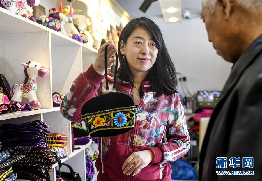 在新疆哈密市一家刺绣手工艺品店内,店主包静(左)向顾客介绍自己设计制作的刺绣工艺品(2019年3月7日摄)。