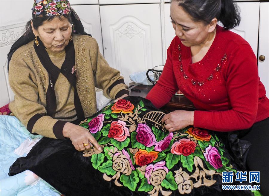 在新疆哈密市,刺绣艺人阿加汗·赛买提(左)和女儿探讨针法(2019年3月6日摄)。